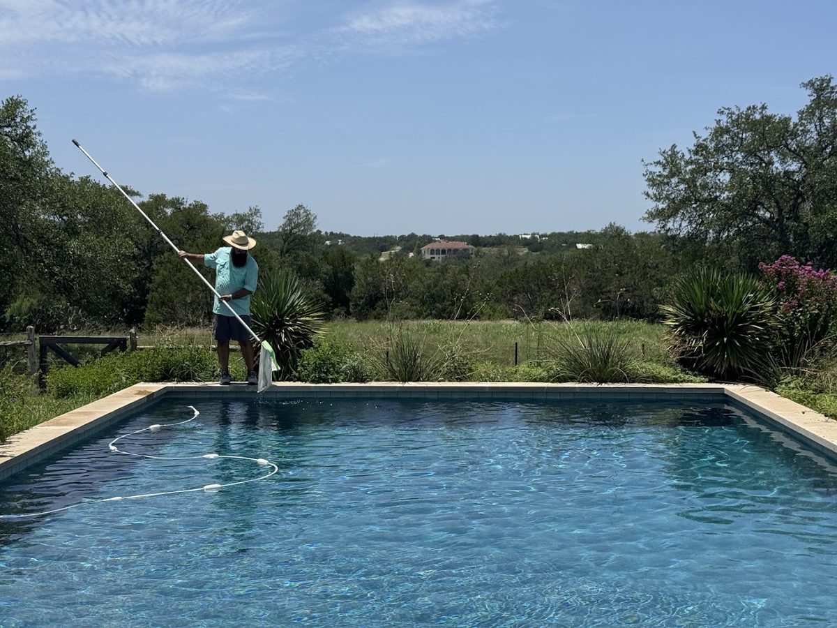 Technician brushing a backyard pool on acreage outside Dripping Springs, TX