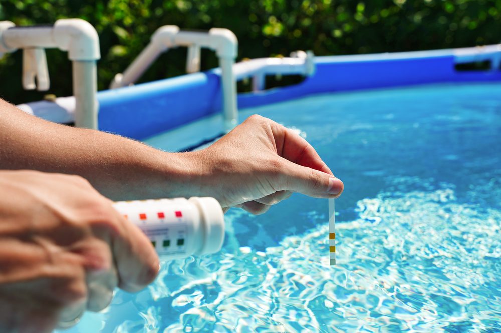Technician testing pool water chemistry with a test kit at the pool edge